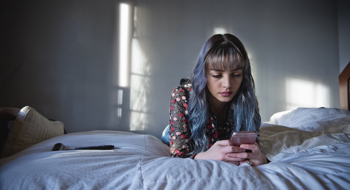 Teen with long hair looks at phone on bed