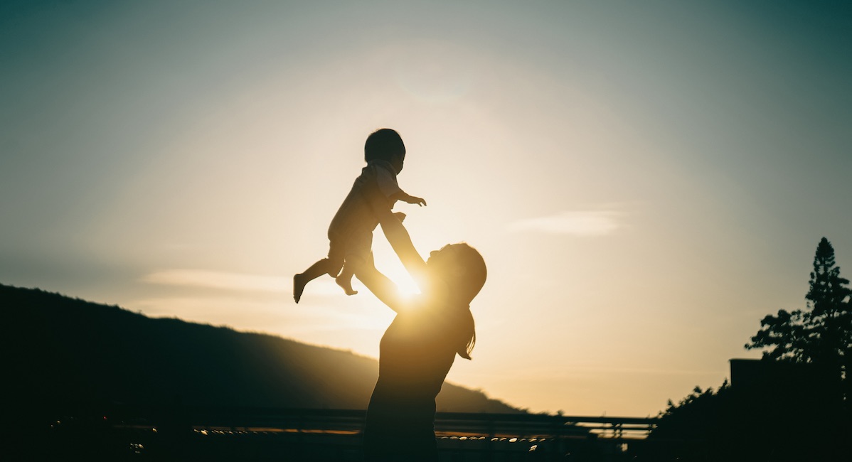 Silhouette of mother raising baby girl in the air outdoors against sky during a beautiful sunset