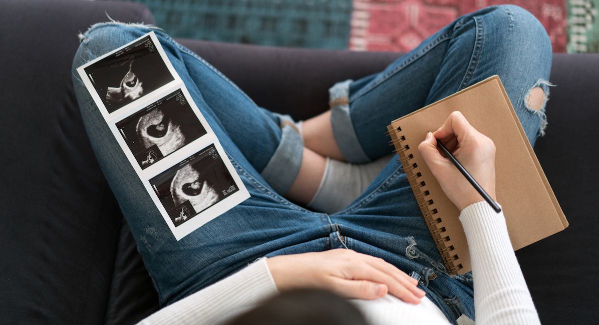 Pregnant woman writing notes to her baby with ultrasound image