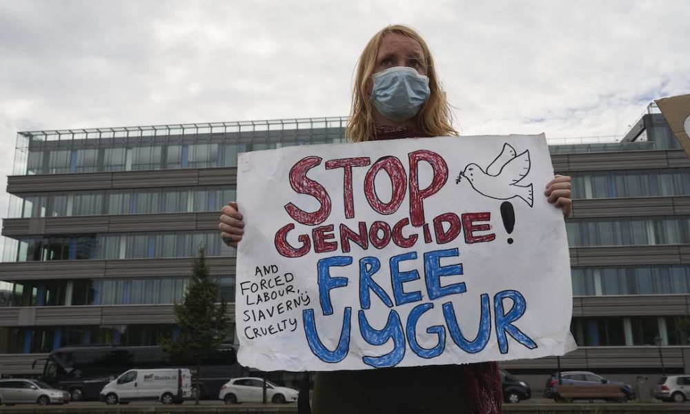 A woman holds a sign stating stop genocide. Organ harvesting, free uyghur. Uyghur, Uighur, Muslims, China, forced genocide.