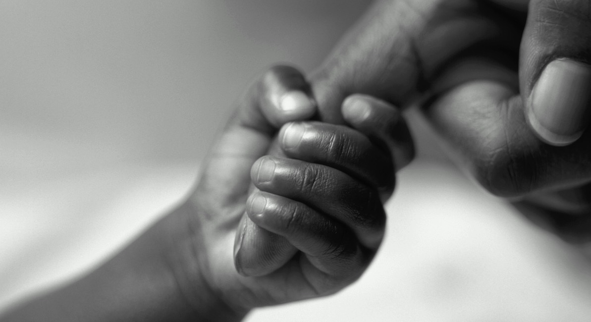 Child’s hand holding onto adult finger, close-up (B&W)