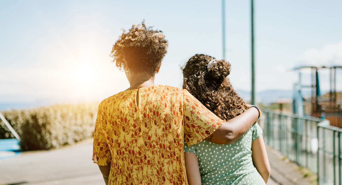 rear view of afro-american mother and daughter embracing in public park