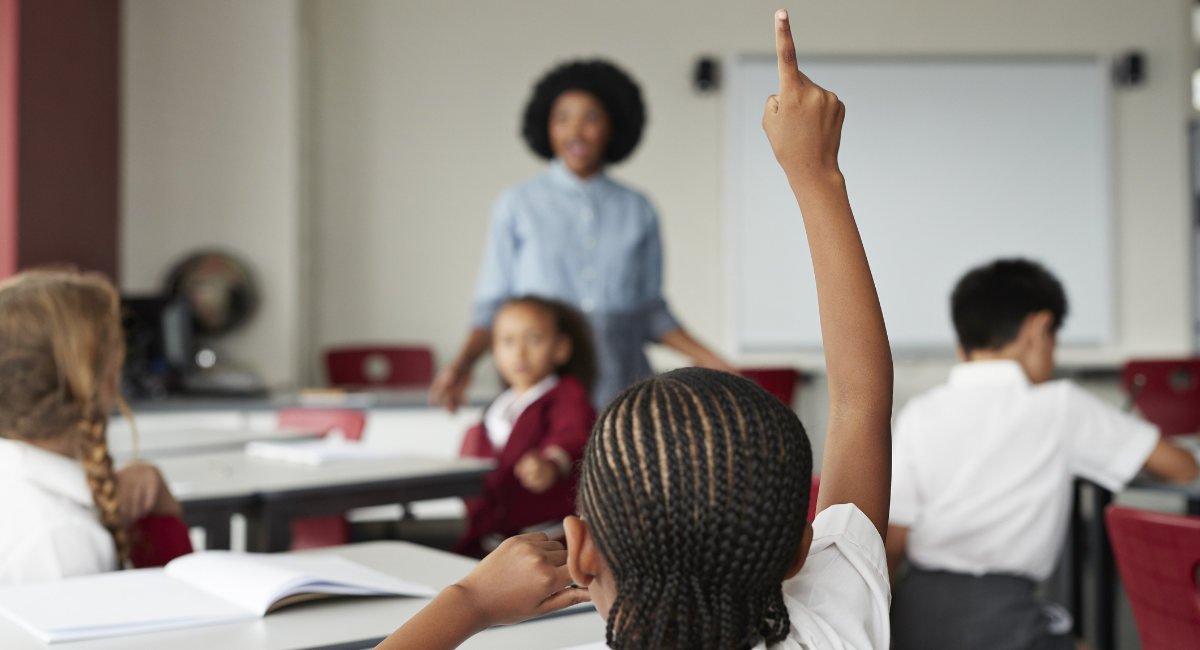 Focus on schoolgirls raised hand in classroom with teacher