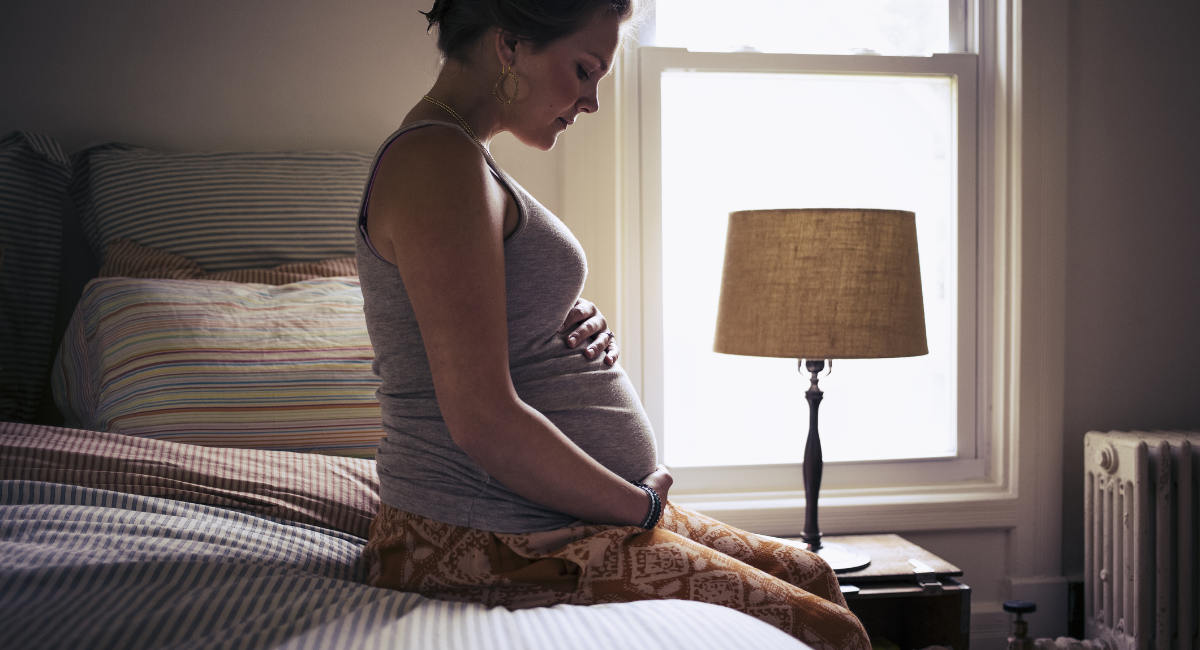 doulas, Pregnant young woman sitting on bed at home