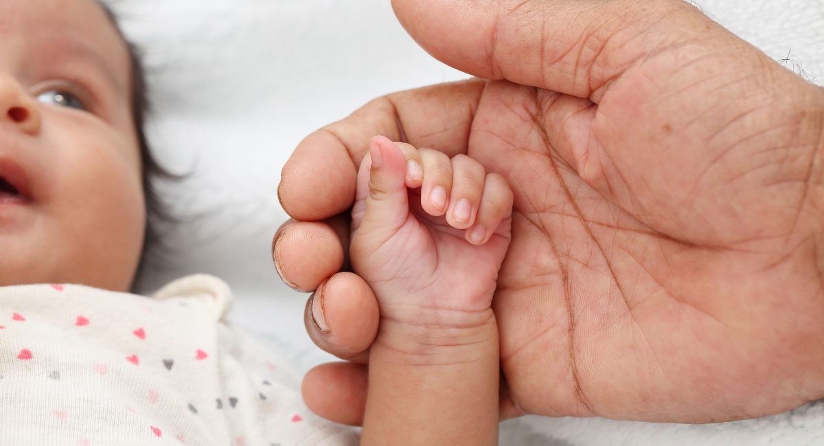 Newborn baby and parent hands together