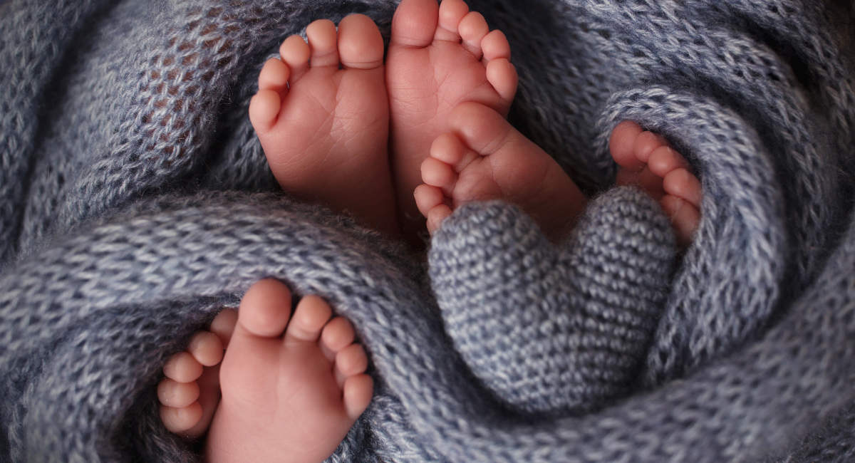 Feet of three newborn babies in a soft blanket. Heart in the legs of newborn triplets. Studio photography.
