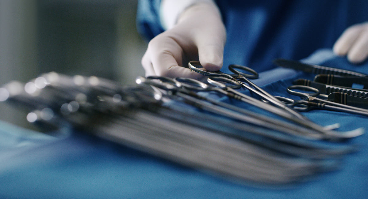Cropped shot of an unrecognizable doctor removing a pair of forceps from a tray of surgical instruments