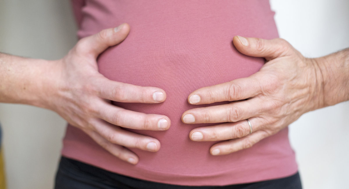 Two hands of different people on the belly of a pregnant woman.