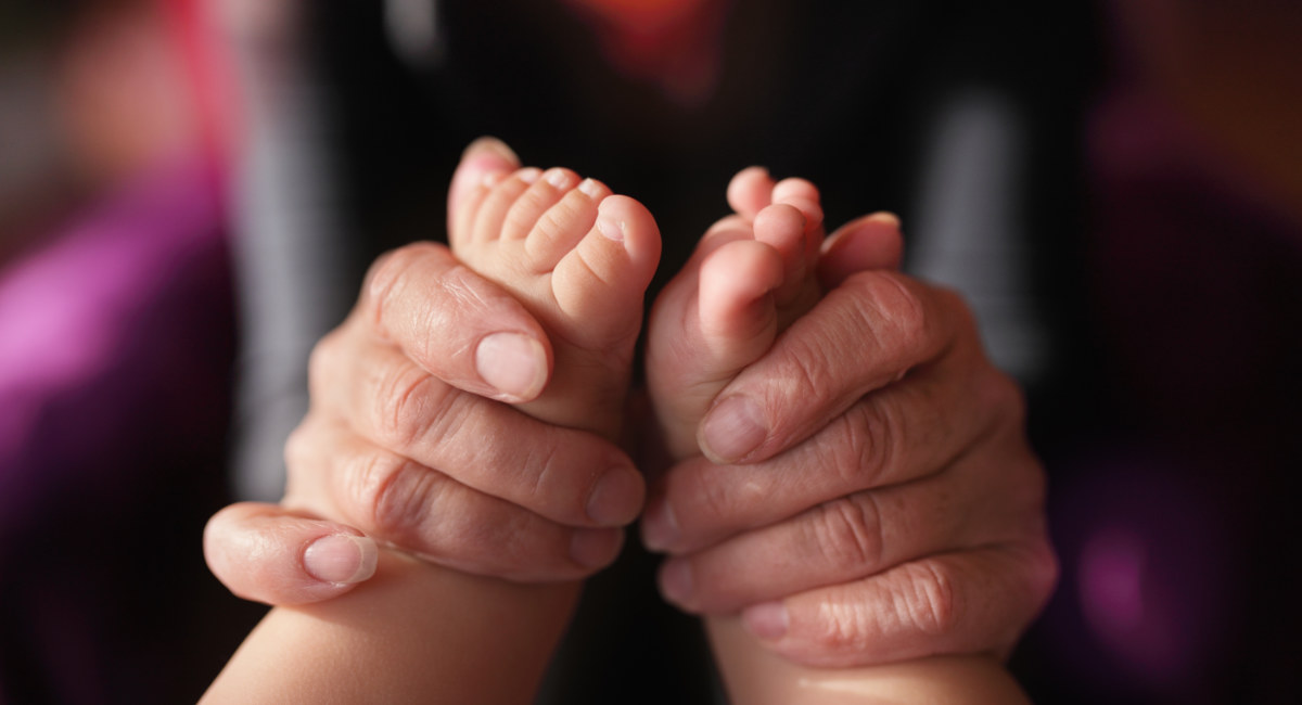 Hands of grandmother holding newborn feets