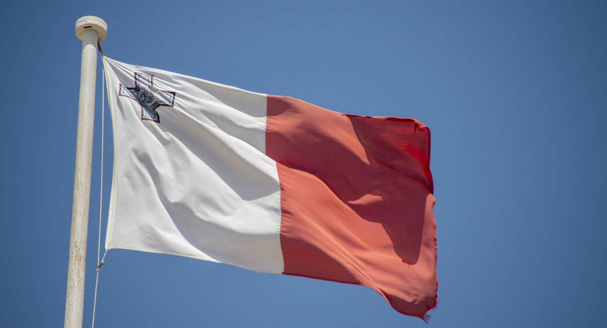 The flag of Malta flying over a clear blue sky.