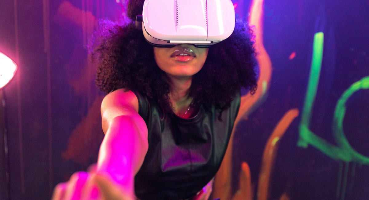 Shocked female wearing VR goggles touching air while experiencing cyberspace in studio with neon illumination