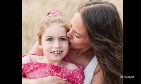 Nine-year-old Charleigh Pollock wearing a pink shirt is held by her mother, who is kissing her on the cheek.