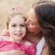 Nine-year-old Charleigh Pollock wearing a pink shirt is held by her mother, who is kissing her on the cheek.