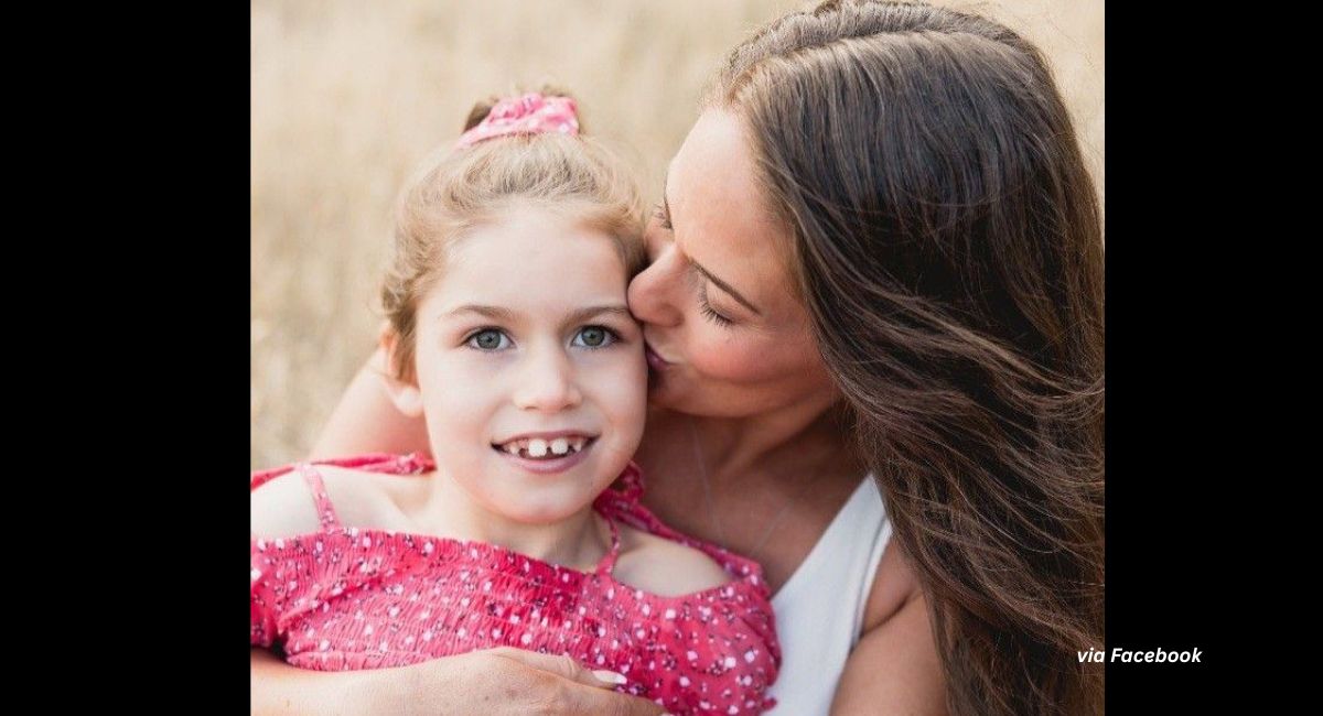 Nine-year-old Charleigh Pollock wearing a pink shirt is held by her mother, who is kissing her on the cheek.